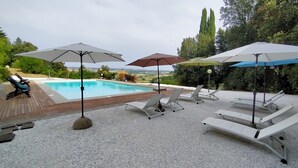 Un área junto a la piscina con sillones de descanso y sombrillas, una terraza de madera y vistas al paisaje.