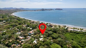 An aerial view of a coastal area with a beach, houses, and a red location marker. - CASA CARAO POTRERO -100 Metros de la Playa (Provincia de Guanacaste)