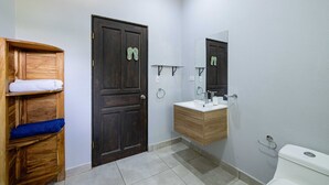 A bathroom with a wooden shelf, a dark door, a white sink with a mirror, and a toilet. - CASA CARAO POTRERO -100 Metros de la Playa (Provincia de Guanacaste)