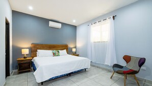 A bedroom with a bed, bedside lamps, a chair, and a window with curtains. - CASA CARAO POTRERO -100 Metros de la Playa (Provincia de Guanacaste)