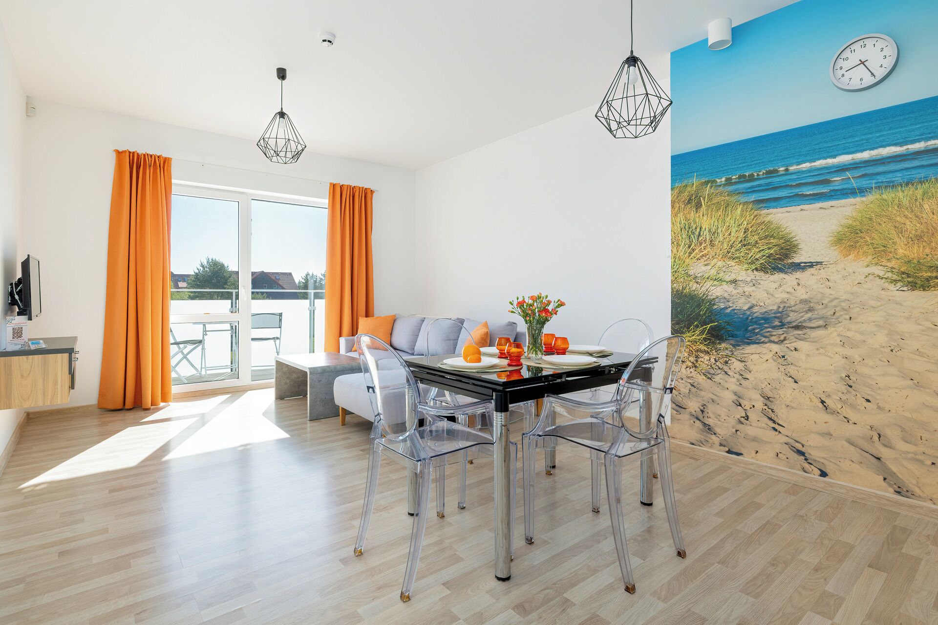 A modern dining area with a glass table and chairs, a sofa, and a beach mural on the wall.