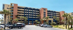 Un hotel de varios pisos con entrada principal, estacionamiento y palmeras.