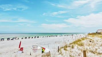 A beach with umbrellas and beach chairs, a lifeguard stand, and a building in the background.