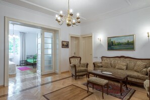 A spacious living room with a wooden floor, a large sofa, a coffee table, and a chandelier.