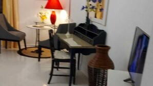 Een kleine, moderne woonkamer met een eettafel, een rode lamp en een grote vaas.