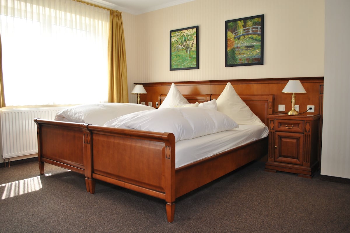A double bed with a wooden frame, two bedside tables with lamps, and two framed pictures on the wall.