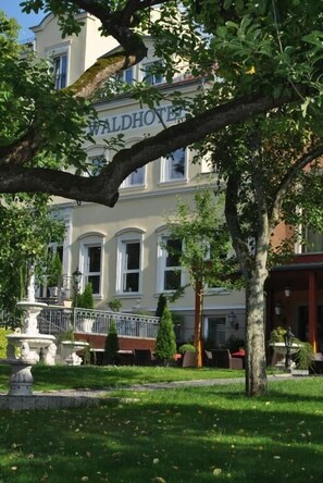 Un hôtel portant l’inscription « WALDHOFEN », entouré d’une végétation luxuriante et d’une pelouse bien entretenue.