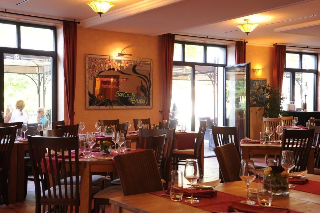 Un restaurante con varias mesas y sillas, ventanas amplias y un letrero en la pared que indica el horario del almuerzo.