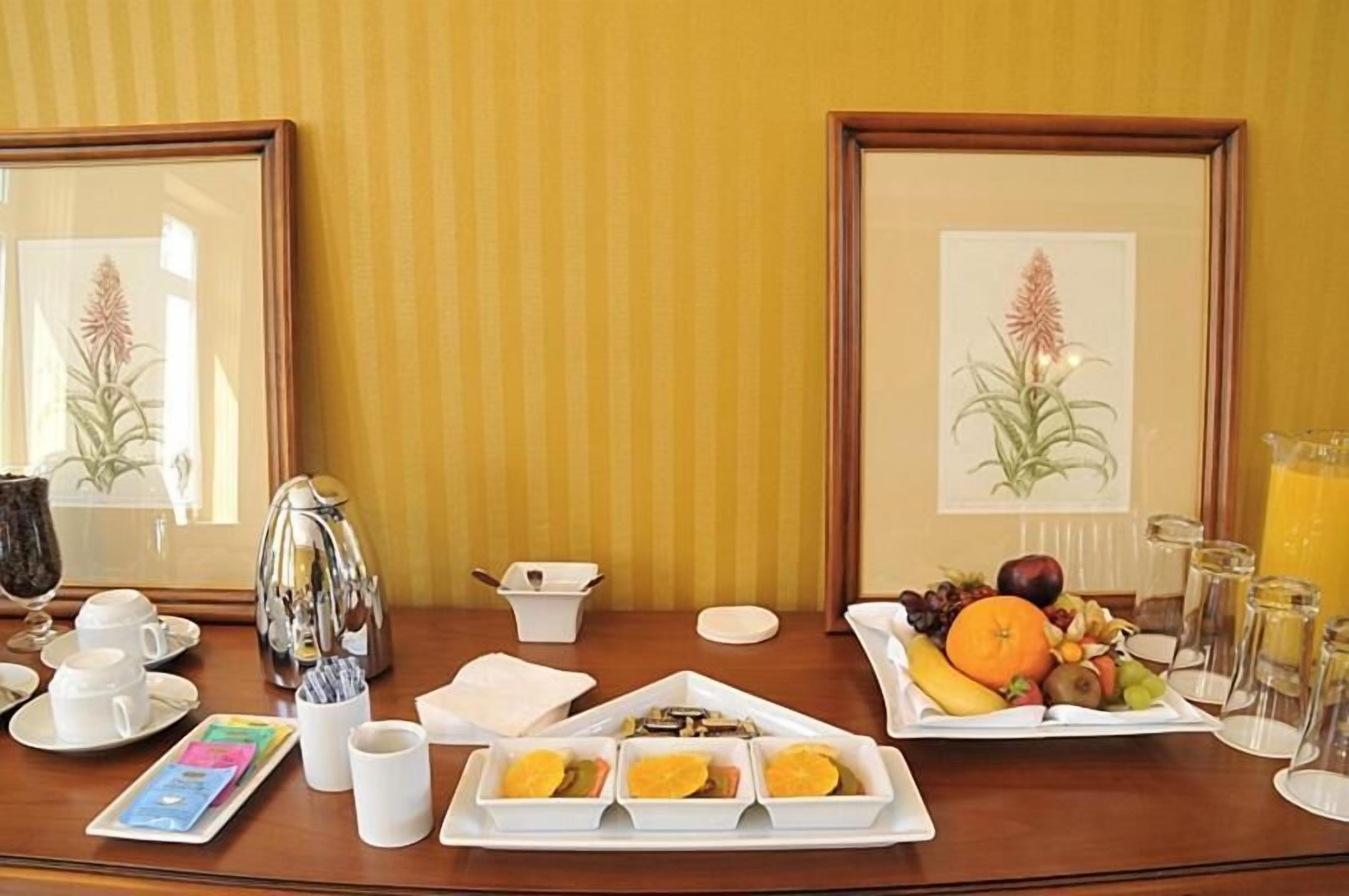 A breakfast setup with a coffee pot, cups, a fruit plate, and a juice pitcher on a wooden table.