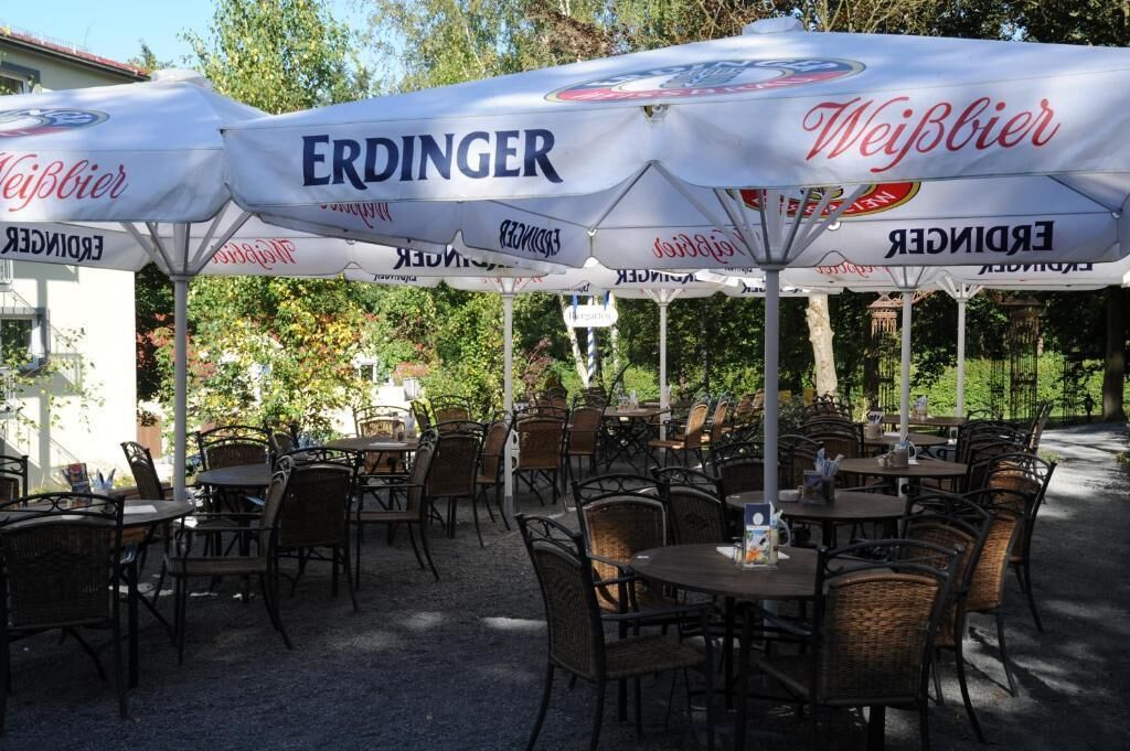 Café al aire libre con mesas y sillas bajo sombrillas con la marca 'ERDINGER' y 'Weißbier'.
