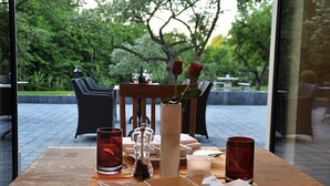 Une table dressée pour deux personnes, avec un vase de roses rouges, un salier et un poivrier, et deux verres rouges.