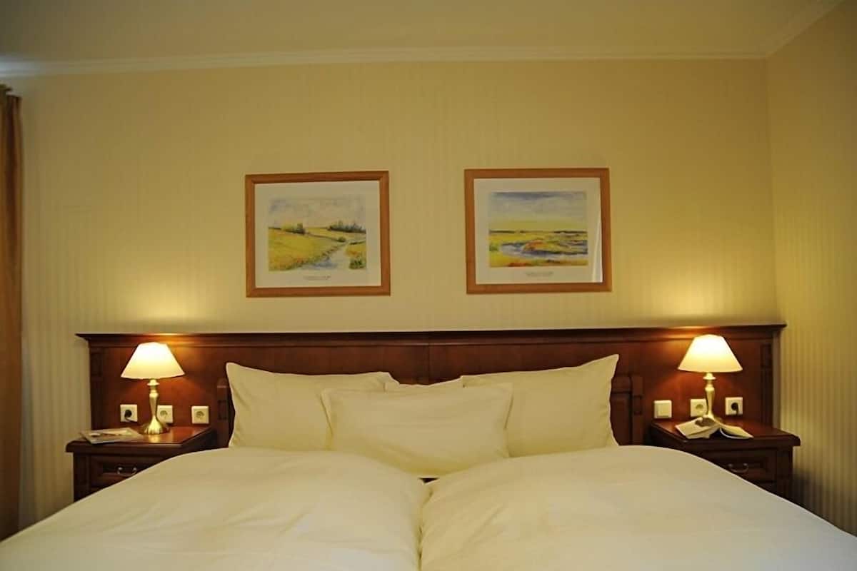 A hotel room with a large bed, two bedside tables with lamps, and two framed landscape paintings on the wall.