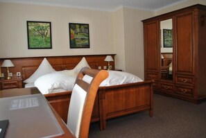 A hotel room with a wooden bed, two bedside tables, a nightstand, a large mirror, and two framed pictures on the wall.