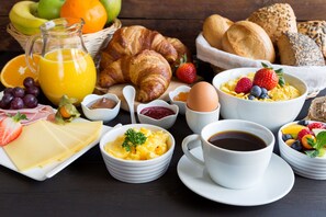 A breakfast setting with croissants, bread, fruits, cheese, eggs, and beverages.
