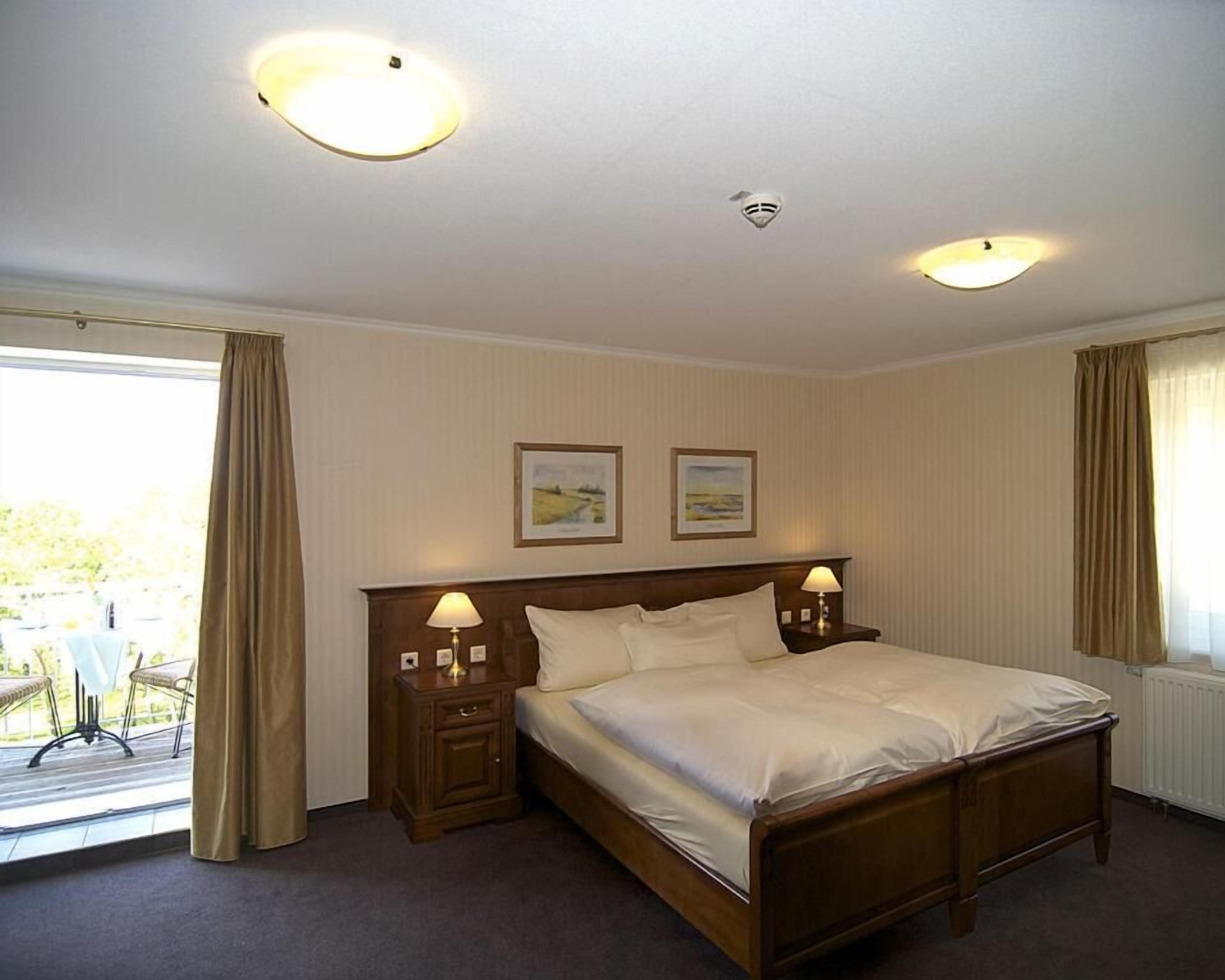 Habitación de hotel con una cama grande, dos lámparas de noche, una ventana con cortinas y dos cuadros en la pared.