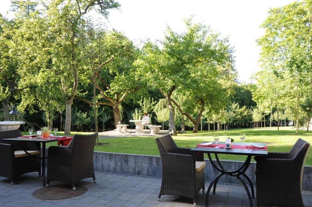 An outdoor patio area with wicker furniture and a stone table, surrounded by lush greenery.