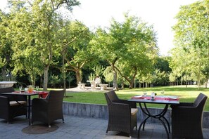 An outdoor patio area with wicker furniture and a stone table, surrounded by lush greenery.