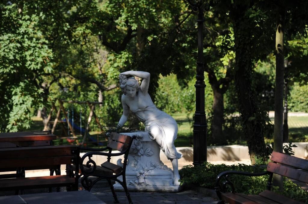Ein Park mit einer Statue einer Frau auf einem Sockel, Bänken und Bäumen.