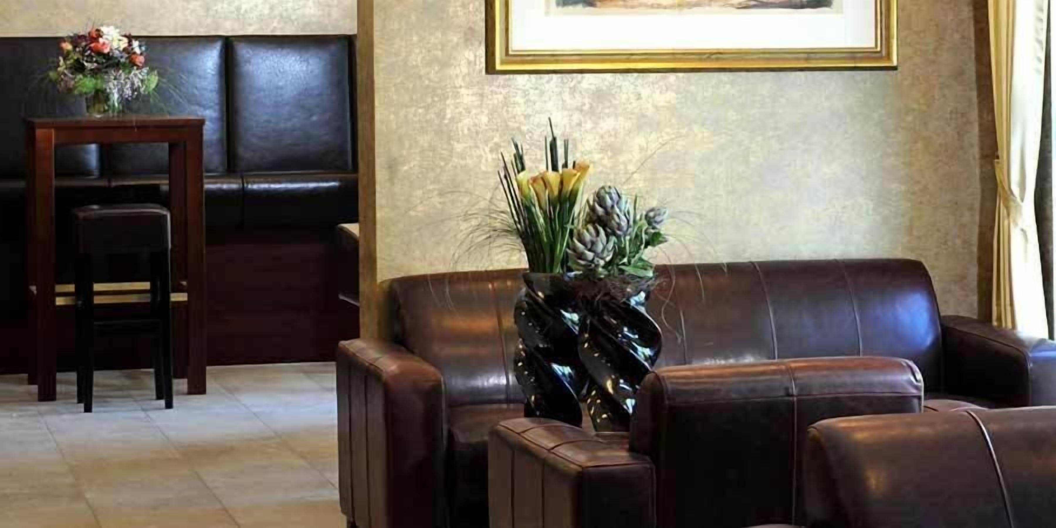 A dark brown leather sofa, a small wooden table with a vase of flowers, and a framed picture on the wall.