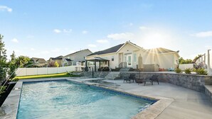 A swimming pool with a stone deck, a covered seating area, and a house in the background.