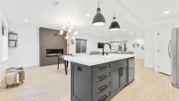 A modern kitchen with a large island, black pendant lights, and a built-in fireplace.