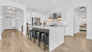 A modern kitchen with white cabinetry, a marble island, black bar stools, and recessed lighting.