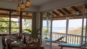 A dining area with a table set for a meal, large windows, and a view of the ocean. - Spacious hideaway with ocean views and fine eatery (00000)