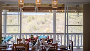 A dining area with a table set for four, large windows with a view of a natural landscape, and hanging wicker lamps. - Spacious hideaway with ocean views and fine eatery (00000)
