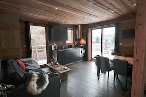 A cozy living room with a sofa, a coffee table, and a fireplace. There is a kitchen area with a sink and a window overlooking a scenic view.