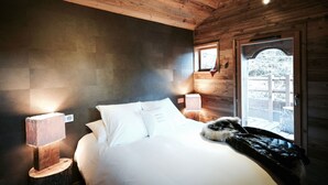 Een slaapkamer in een houten chalet met een bed, twee bedlampjes, een raam en een deur.