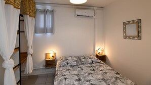 Une chambre à coucher comprenant un lit, deux lampes de chevet, un lustre, un appareil de climatisation, un miroir et des rideaux.