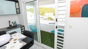 Une cuisine moderne équipée d’un évier, d’un plan de travail et de chaises. Une porte-fenêtre coulissante donne accès à un espace extérieur avec une pelouse verdoyante et des chaises.
