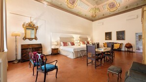 Un'ampia stanza con un letto grande, un tavolo da pranzo con sedie, un camino e un soffitto decorato con elementi artistici.