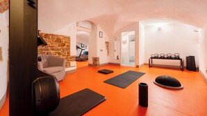 Una stanza spaziosa con una parete in pietra, un divano grigio e tappetini da ginnastica su un pavimento arancione.