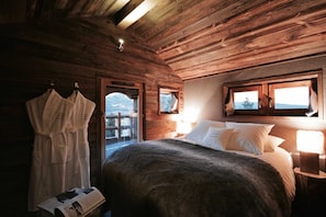 Een slaapkamer in een houten chalet, met een bed, een badjas en een raam met uitzicht.