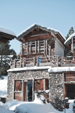 Een rustiek houten chalet met een stenen fundering, een houten balkon en een besneeuwde omgeving.