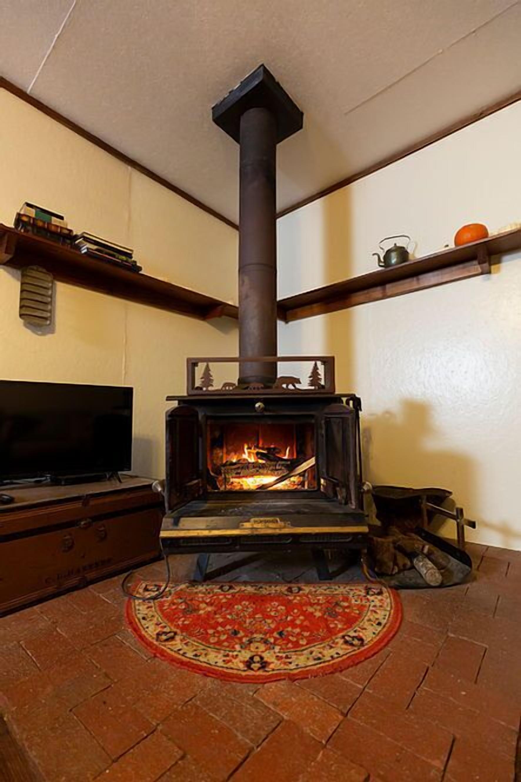 A cozy living room with a wood-burning stove, a television, and a patterned rug on the floor.