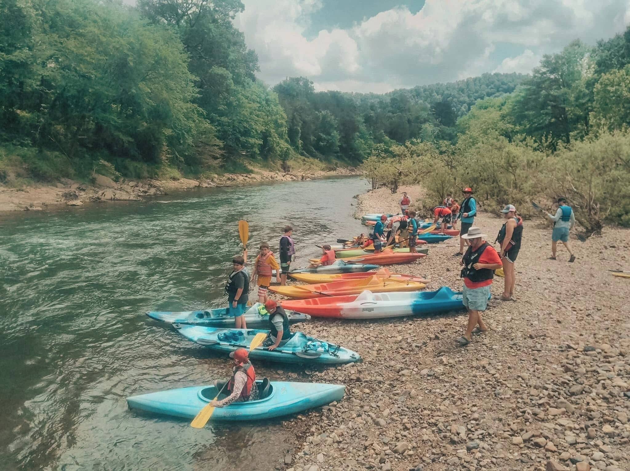 A group of people on a riverbank with kayaks.