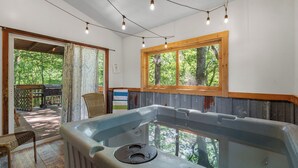 Ein Whirlpool in einem Raum mit Holzwänden, einem Fenster mit Blick auf Bäume und Lichterketten.