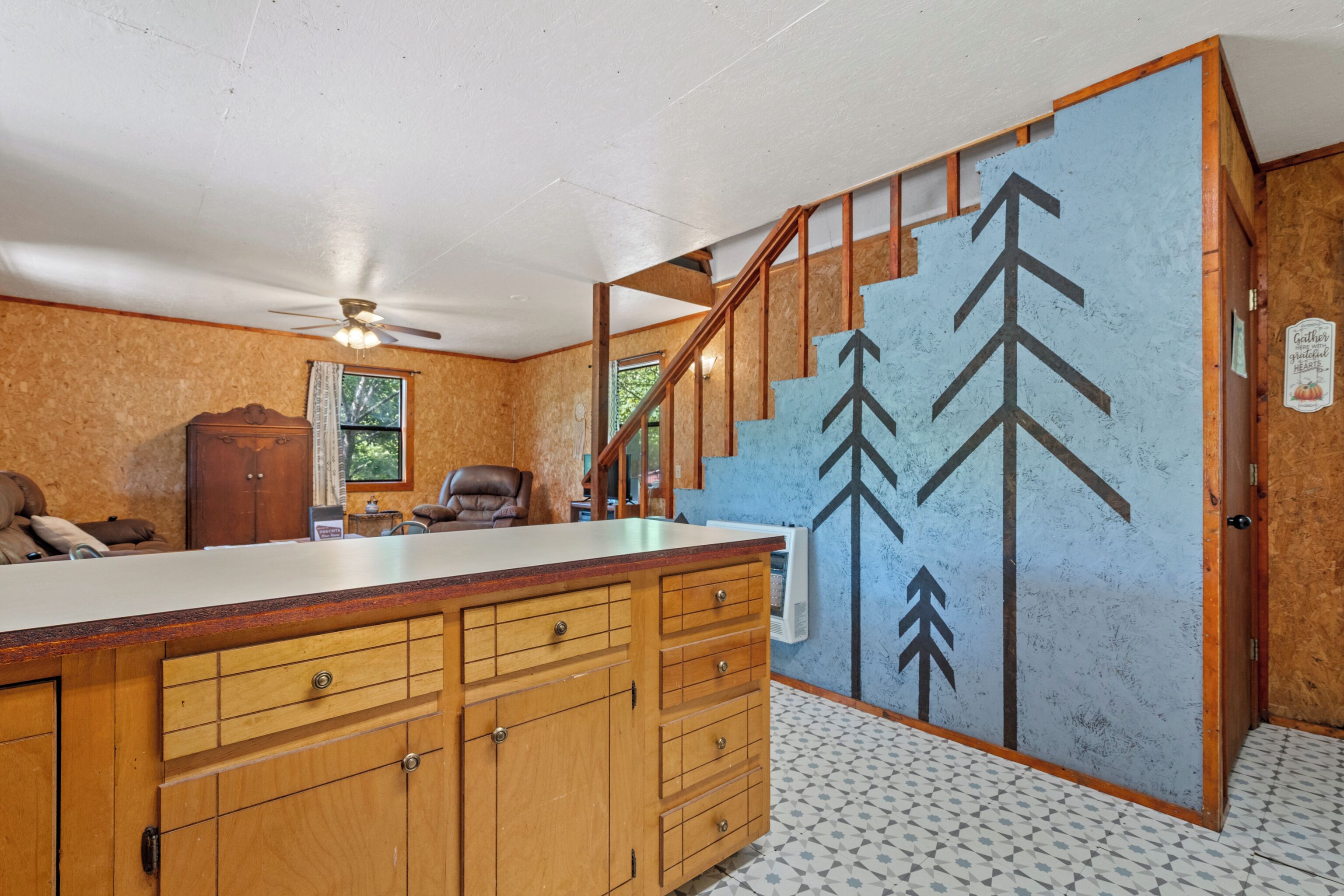 Una cocina con armarios de madera, encimera blanca y pared azul con un mural de un árbol.