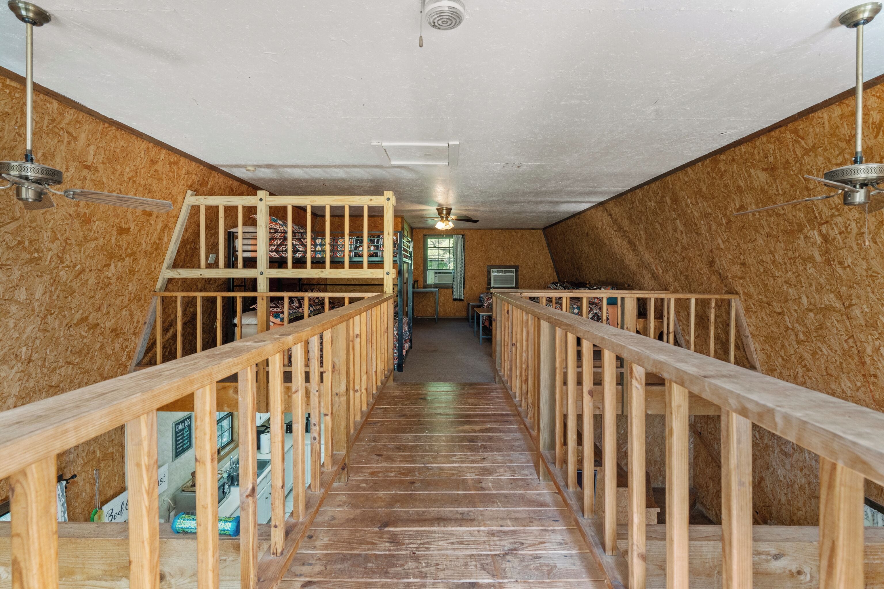 A wooden staircase with a loft area, a ceiling fan, and a TV in a room with wooden walls.