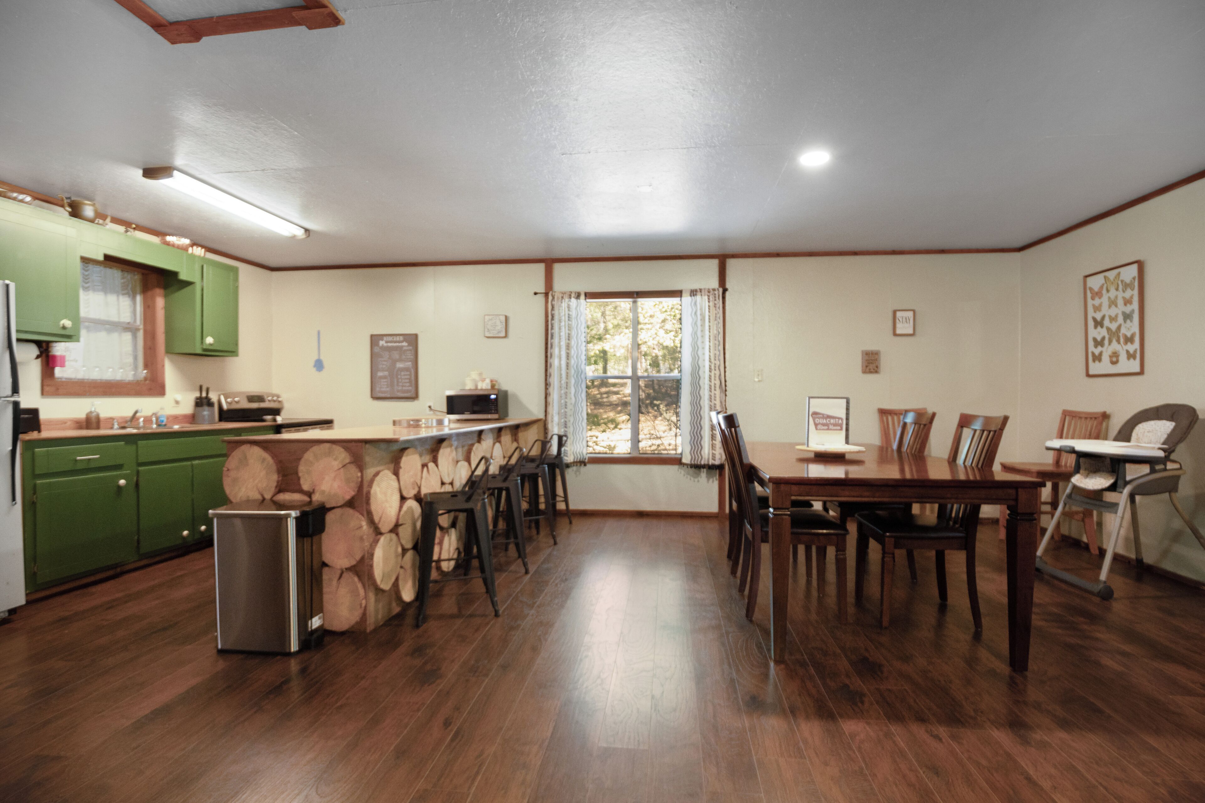 A spacious kitchen with wooden flooring, green cabinets, and a dining area with chairs and a table.