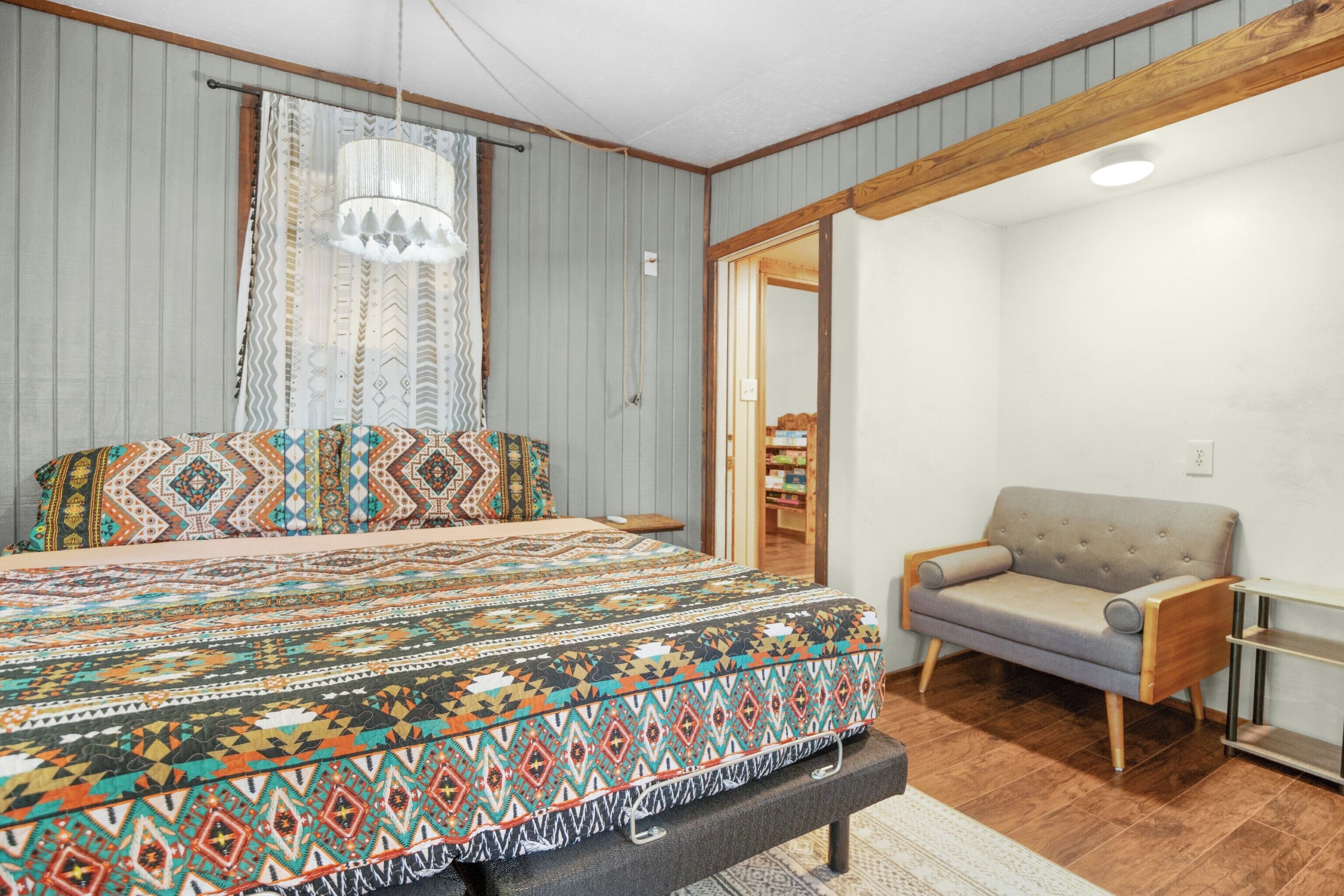Une chambre à coucher comprenant un lit, un banc, un canapé, un lustre et une porte donnant sur une autre pièce.