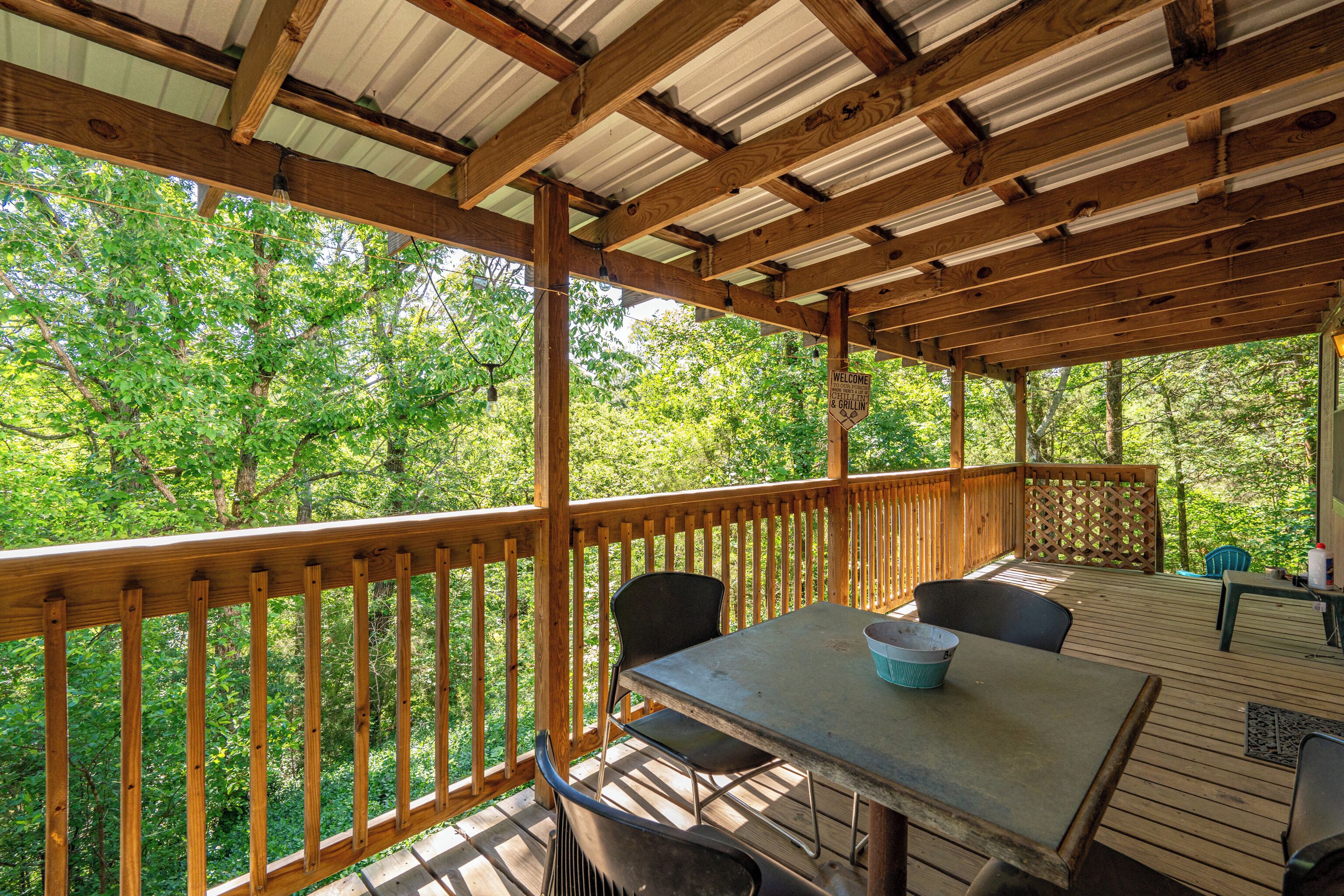 A wooden deck with a table and chairs, surrounded by a wooden railing, overlooking a forested area.