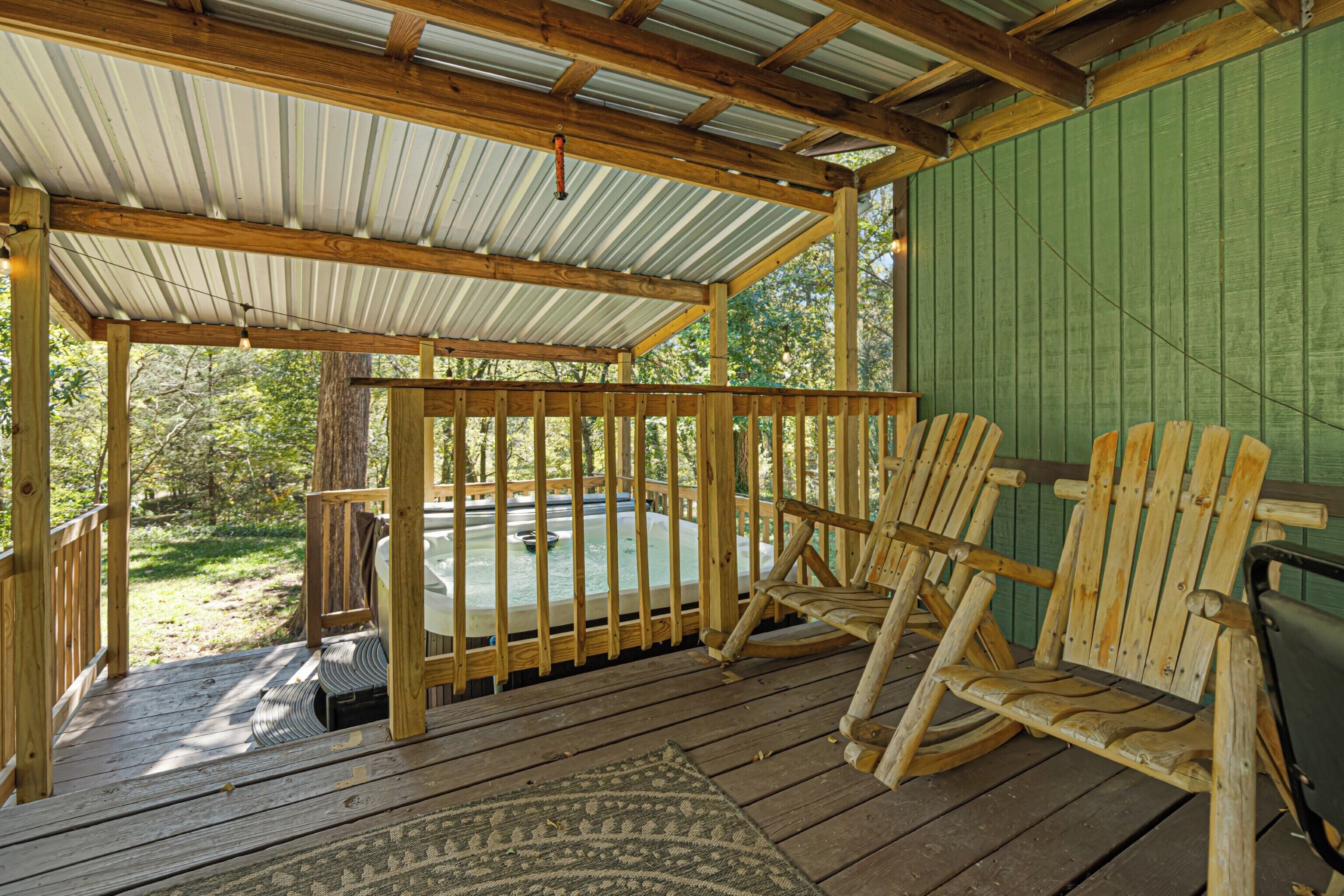 A wooden deck with a hot tub, wooden chairs, and a covered area with a metal roof.