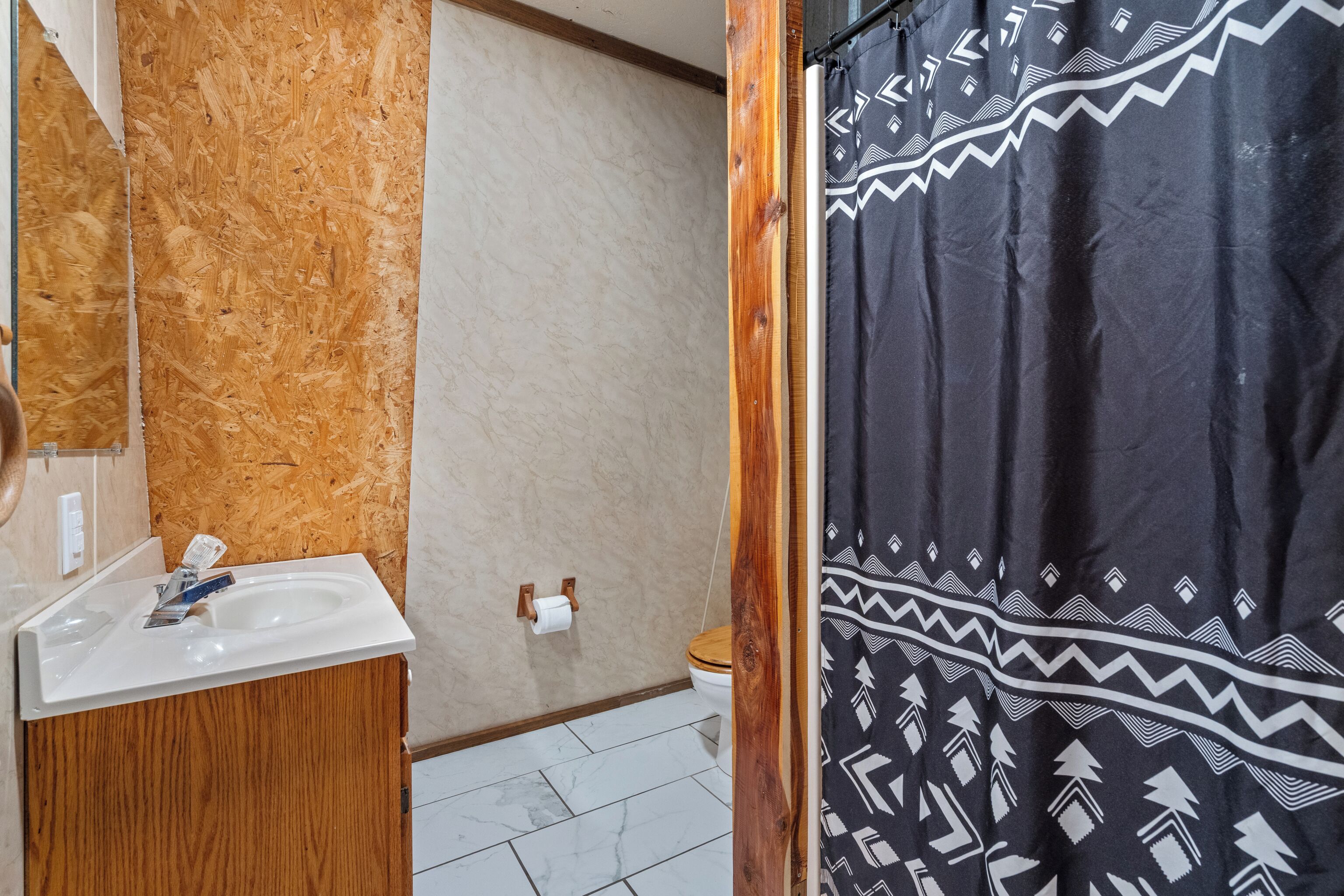 A bathroom with a wooden vanity, a white sink, a toilet, and a shower curtain with a geometric pattern.