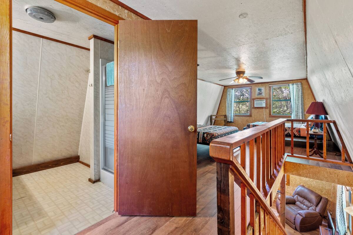 Una habitación con puerta de madera, ventilador de techo, ventana con vistas e una escalera.