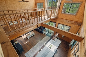 Um amplo loft com teto alto, escada de madeira, área de jantar com mesa comprida e grandes janelas com vista para o exterior.