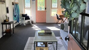 Una habitación acogedora con un ventanal grande, un ventilador de techo, una cesta de mimbre sobre una mesa y una puerta con un cartel.