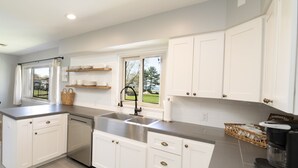 Una cocina moderna con muebles blancos, un lavamanos de acero inoxidable y una ventana con vistas al exterior.
